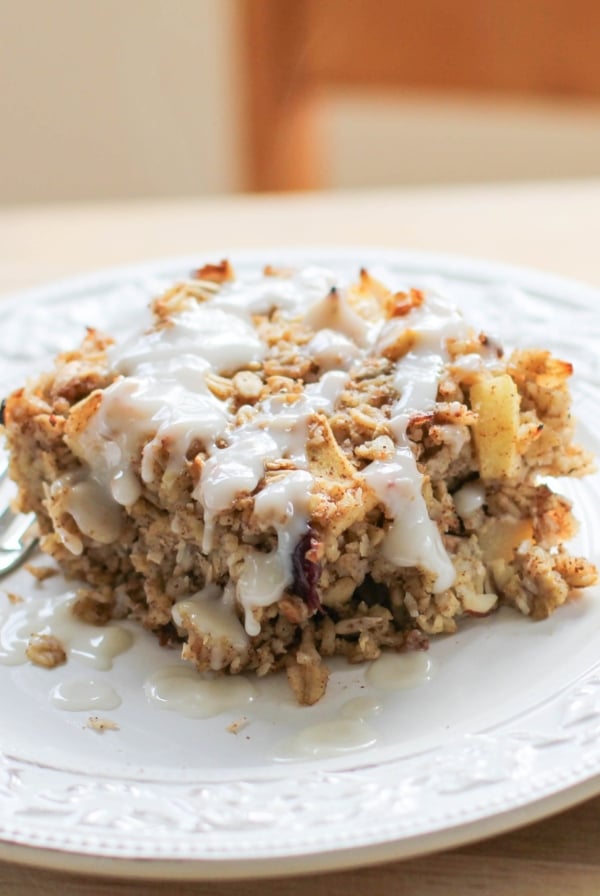 Thick slice of apple baked oatmeal sitting on a plate, drizzled with a glaze. Ready to eat.