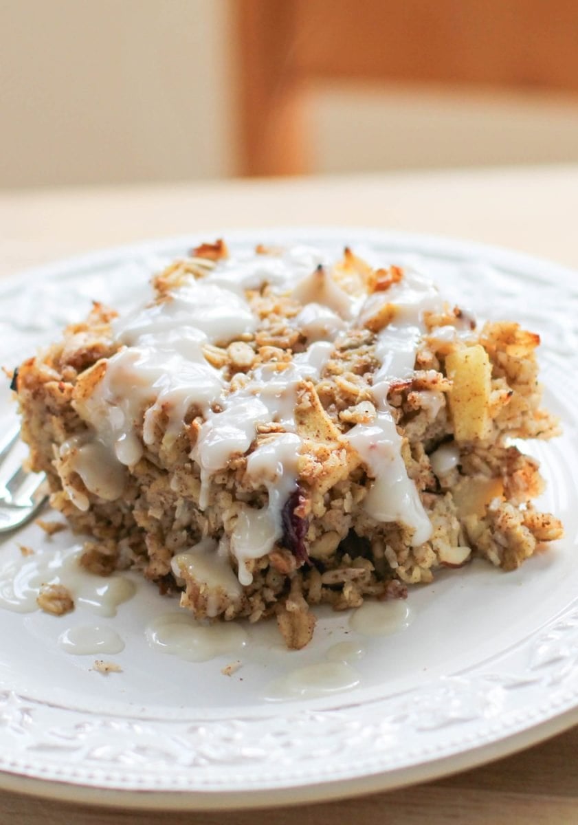 Thick slice of apple baked oatmeal sitting on a plate, drizzled with a glaze. Ready to eat.