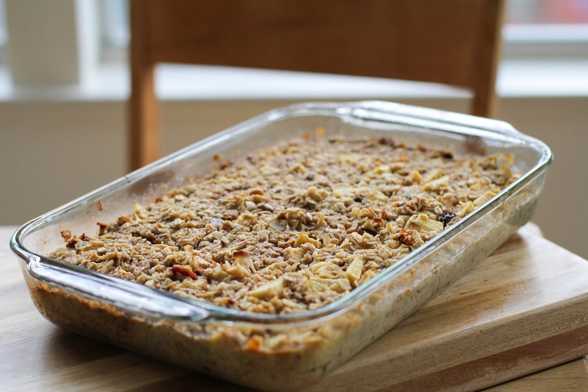 Casserole dish full of apple baked oatmeal sitting on a wooden cutting board, ready to serve.