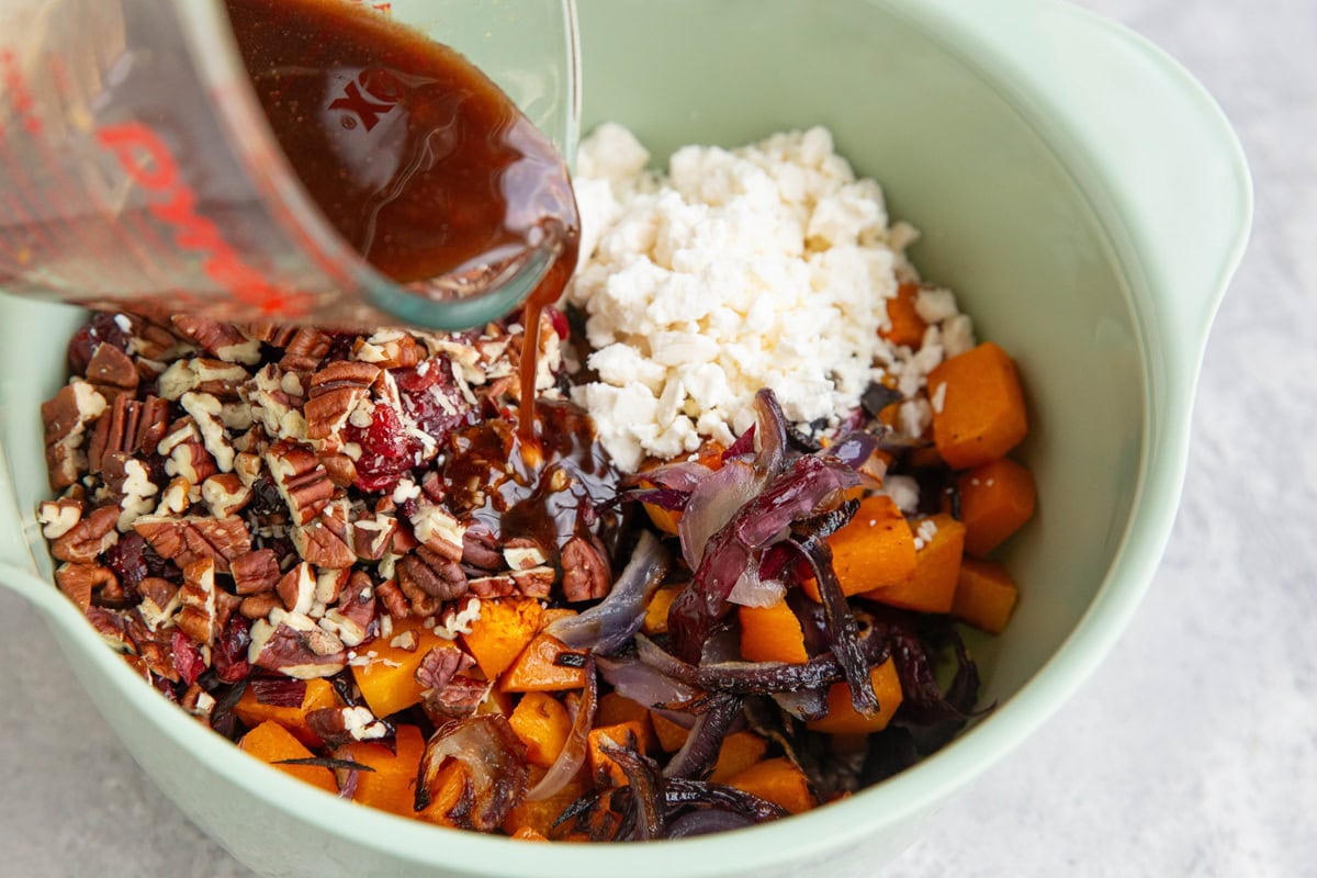 Pouring balsamic vinaigrette into the bowl with the lentils and roasted veggies.