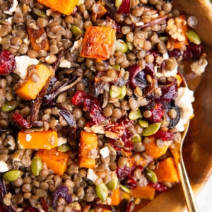 Butternut squash and lentil salad in a large wooden bowl with a golden spoon, ready to serve.