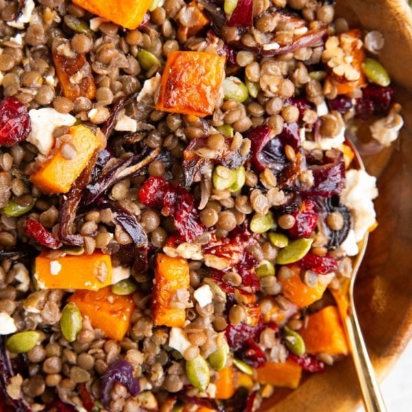 Butternut squash and lentil salad in a large wooden bowl with a golden spoon, ready to serve.