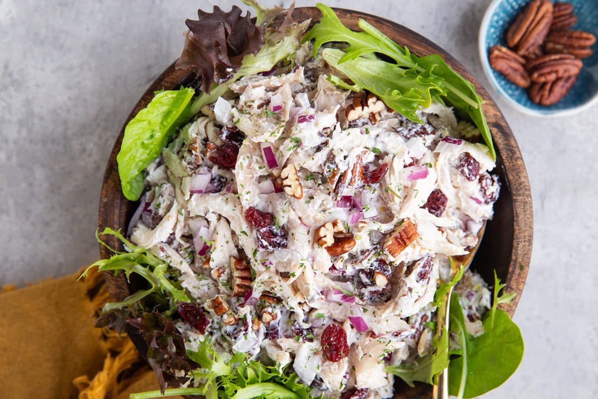 Wooden bowl full of turkey salad with spring greens around and a golden spoon ready to serve.