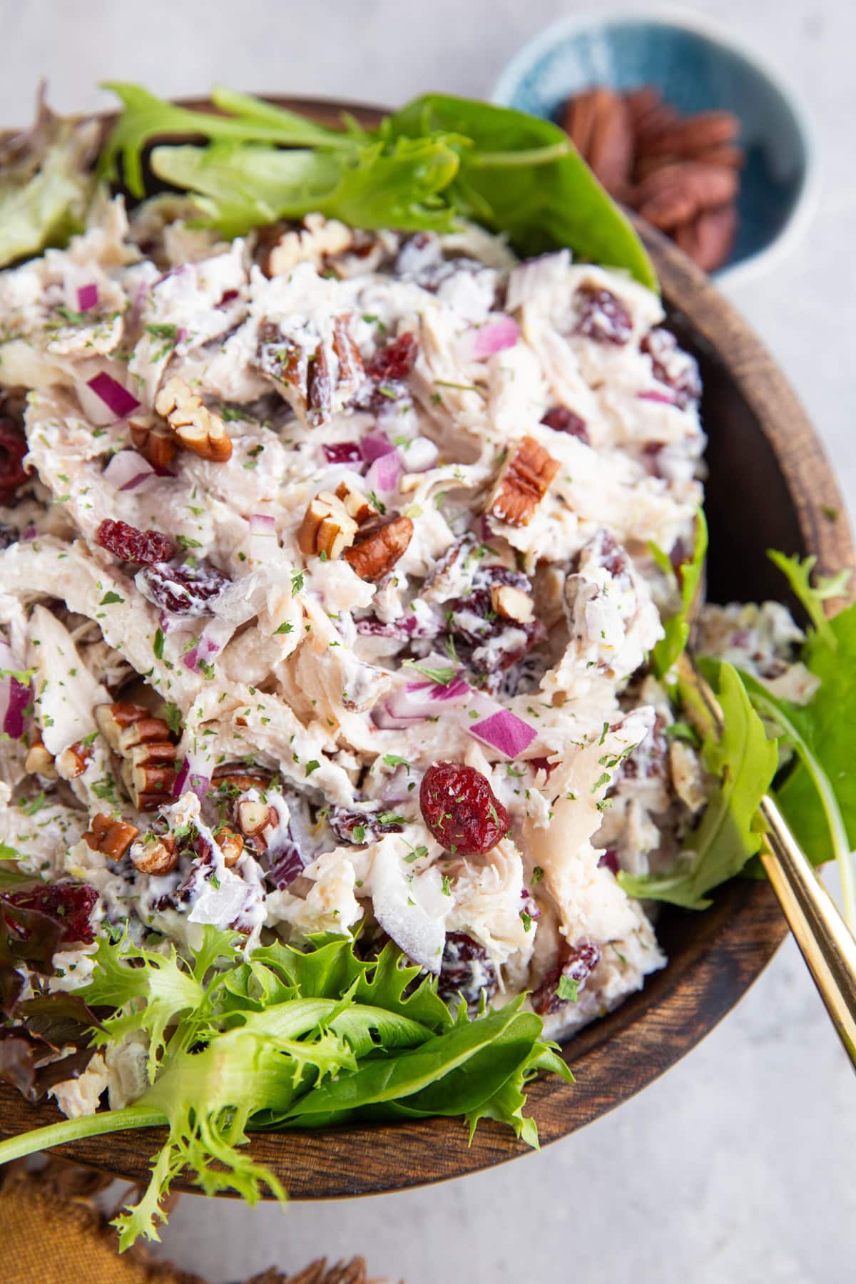 Turkey salad with fresh greens in a wooden bowl with a small bowl of pecans in the background. Ready to use.