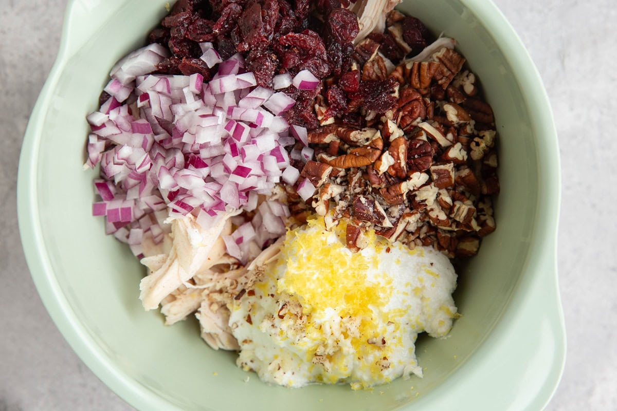 Mixing bowl full of shredded turkey, pecans, dried cranberries, red onion, Greek yogurt, and lemon zest. Ready to be mixed up to make leftover turkey salad
