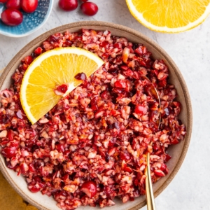 Cranberry relish in a bowl with a slice of orange and a half orange to the side.