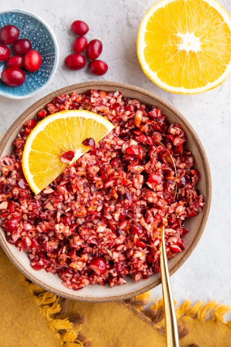Cranberry relish in a bowl with a slice of orange and a half orange to the side.
