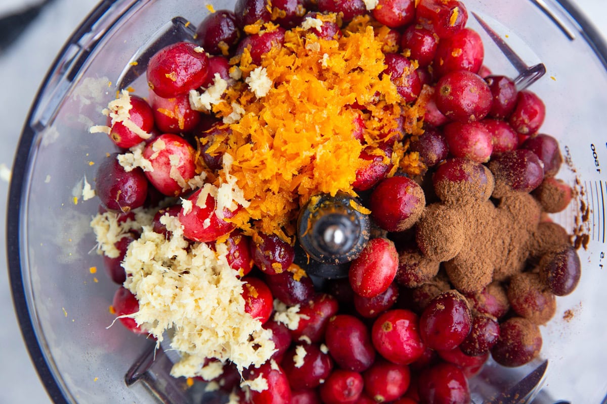 Food processor full of cranberries, orange zest, ginger, and ground cinnamon.