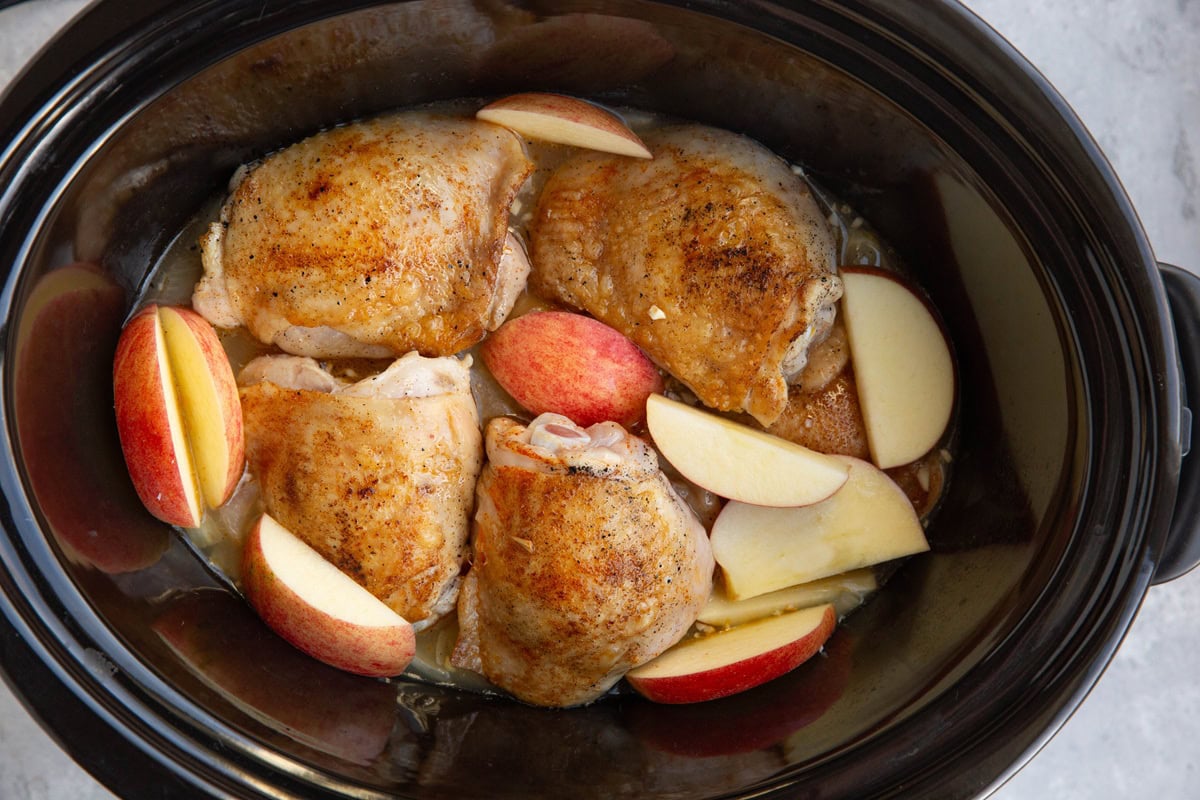Crock pot with chicken, apple cider, chopped apples and onion, ready to cook.