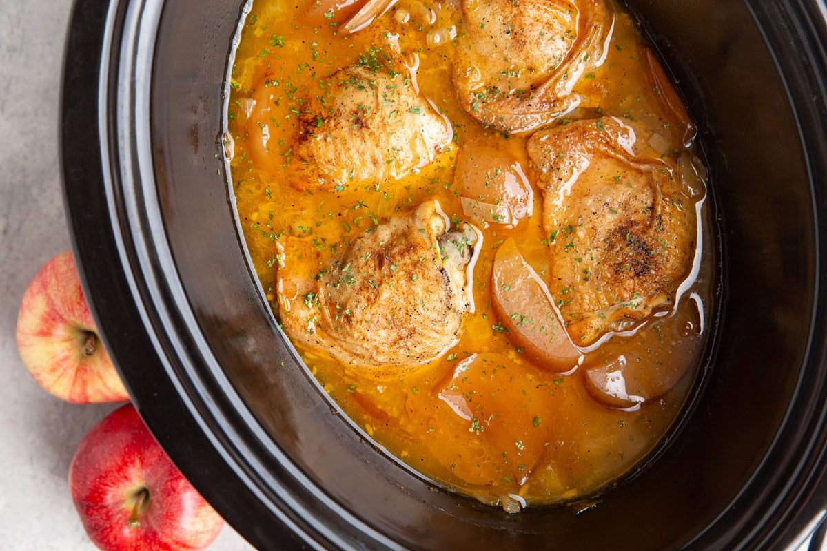 Slow cooker full of cooked chicken thighs and apples in apple cider. Ready to serve.