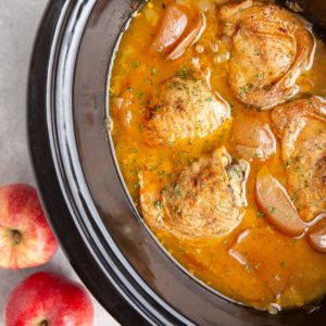 Slow cooker full of bone in chicken thighs, chopped apples, onion, and apple cider surrounding the cooked chicken.