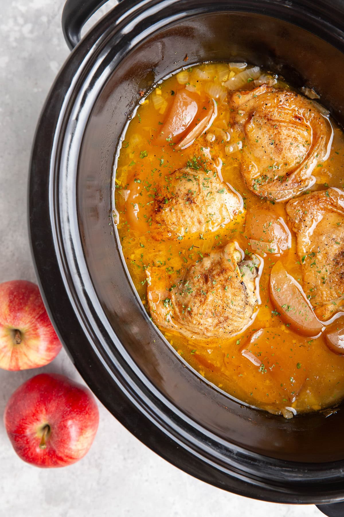 Slow cooker full of bone in chicken thighs, chopped apples, onion, and apple cider surrounding the cooked chicken.
