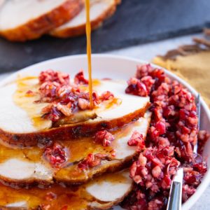 Slices of turkey roast with cranberry relish on top and pan juices being drizzled on top of the meat.