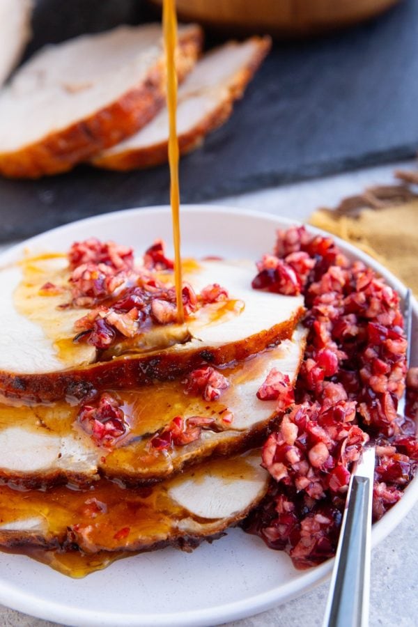Slices of turkey roast with cranberry relish on top and pan juices being drizzled on top of the meat.