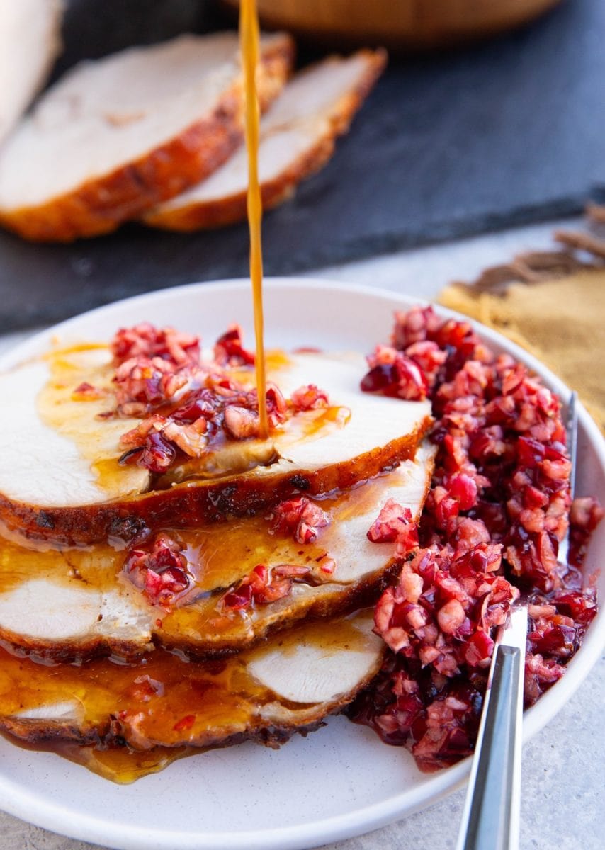 Slices of turkey roast with cranberry relish on top and pan juices being drizzled on top of the meat.