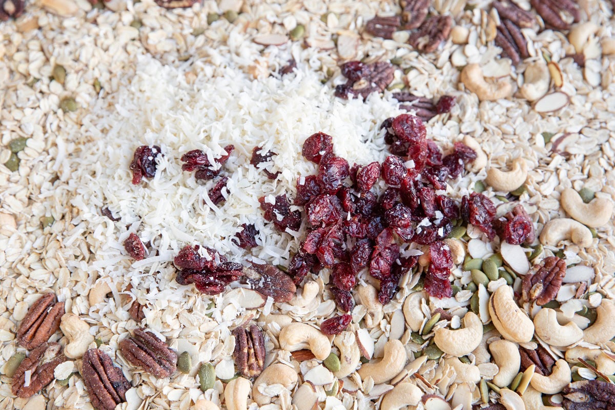 Shredded coconut and dried cranberries on top of a toasted muesli mixture on a baking sheet, ready to be mixed in.