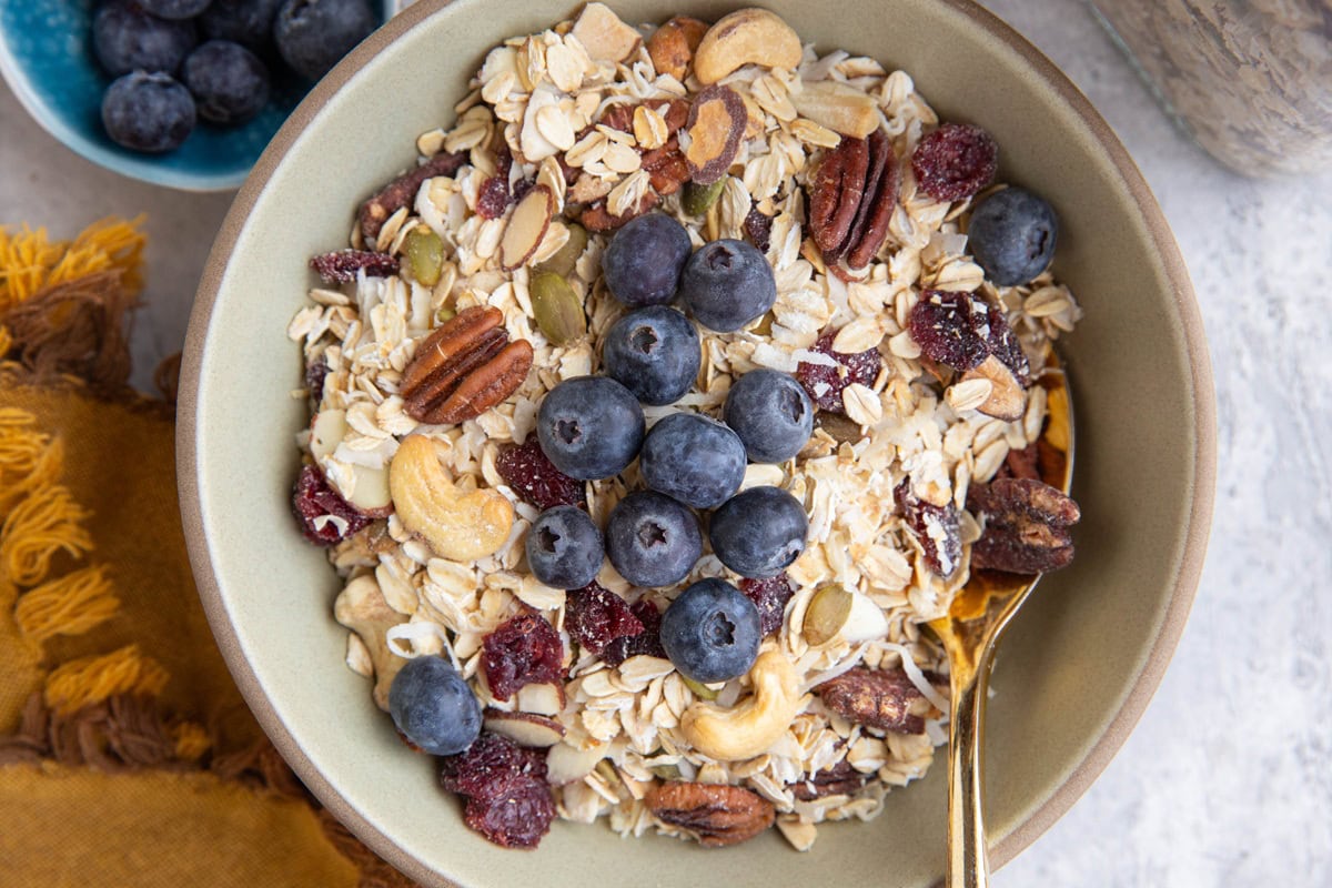 Bowl full of muesli with fresh blueberries on top and a golden spoon, ready to enjoy.