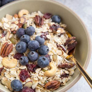 Bowl full of muesli with fresh blueberries on top and a spoon inside the bowl, ready to eat.