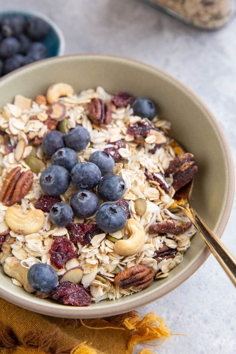 Bowl full of muesli with fresh blueberries on top and a spoon inside the bowl, ready to eat.