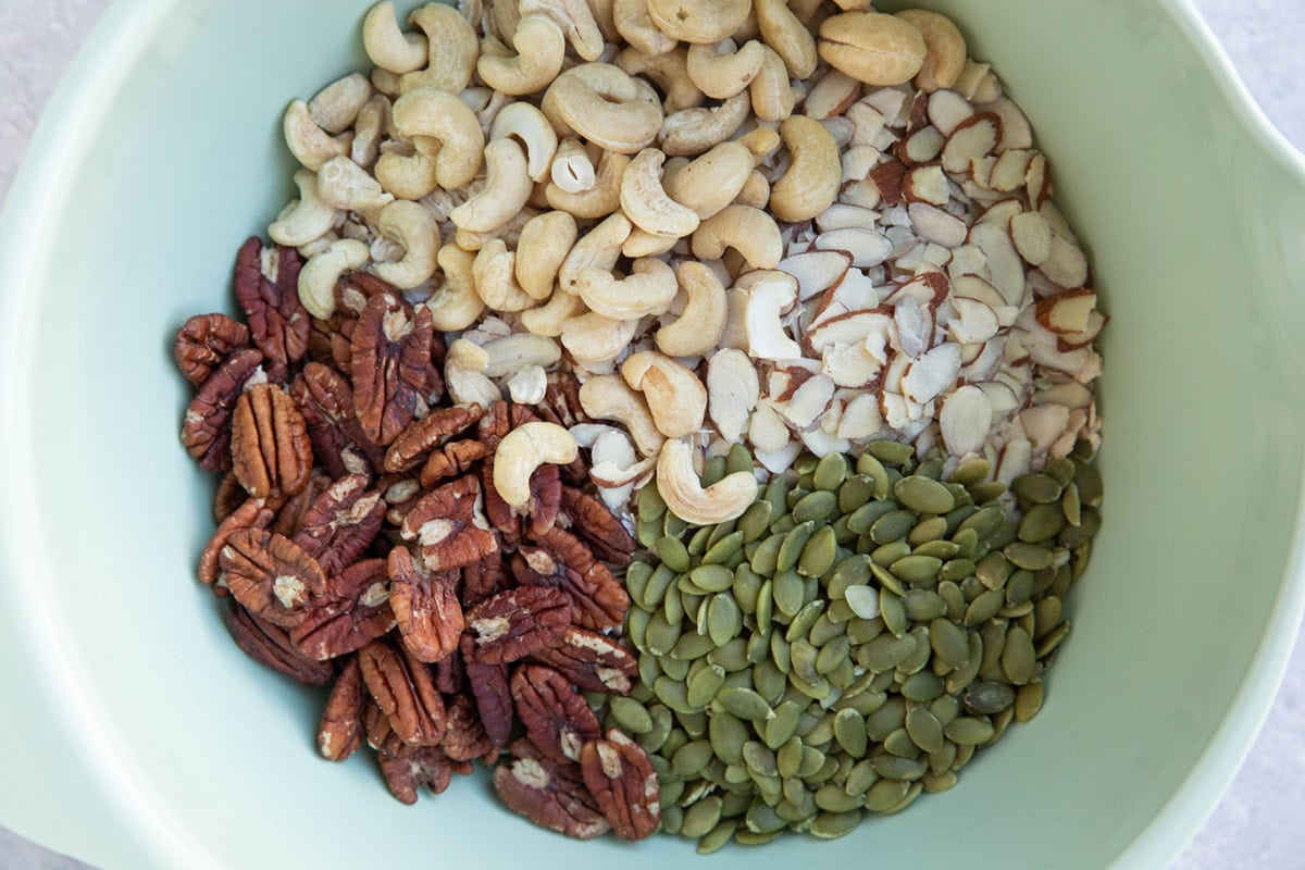 Mixing bowl with oats, cashews, sliced almonds, pecans, and pumpkin seeds, ready to be mixed up