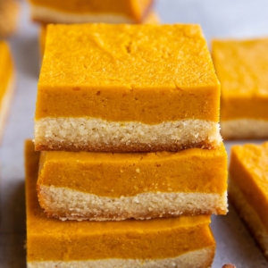 Stack of kabocha squash bars with more bars in the background and cinnamon sticks to the side.