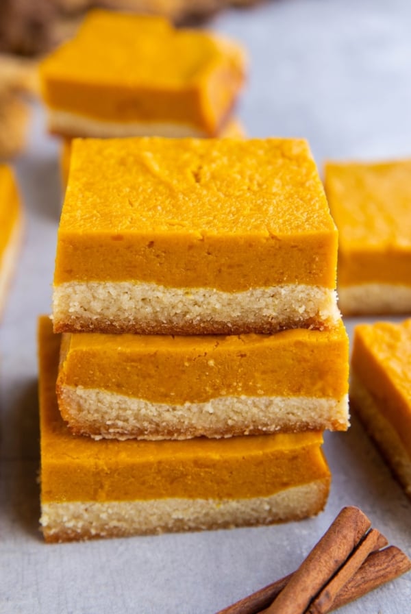 Stack of kabocha squash bars with more bars in the background and cinnamon sticks to the side.