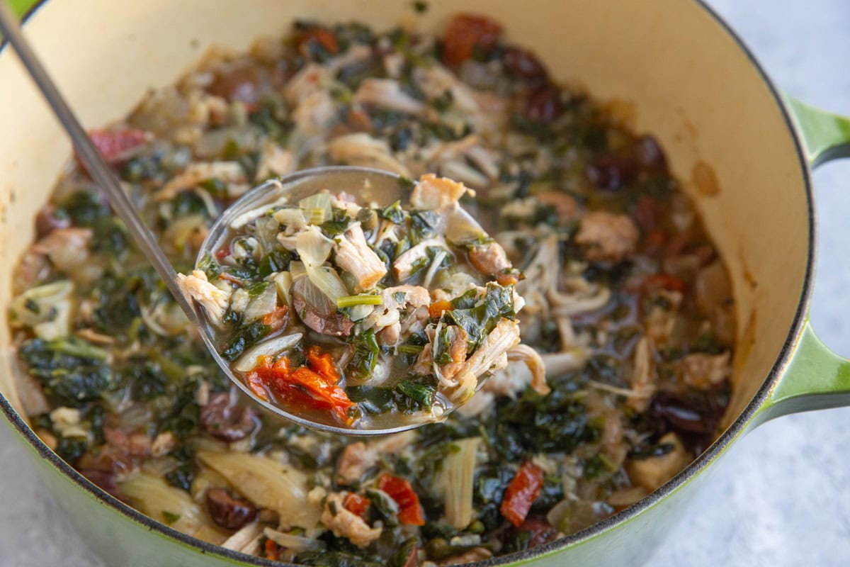 Large pot full of Mediterranean chicken soup with artichoke hearts, sun-dried tomatoes, kalamata olives, brown rice, spinach, etc.
