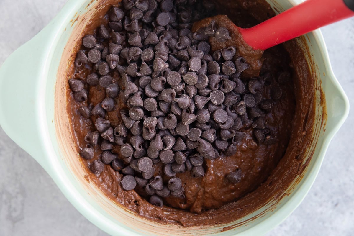 Mixing bowl with chocolate cake batter and chocolate chips on top of the batter, ready to be mixed in.