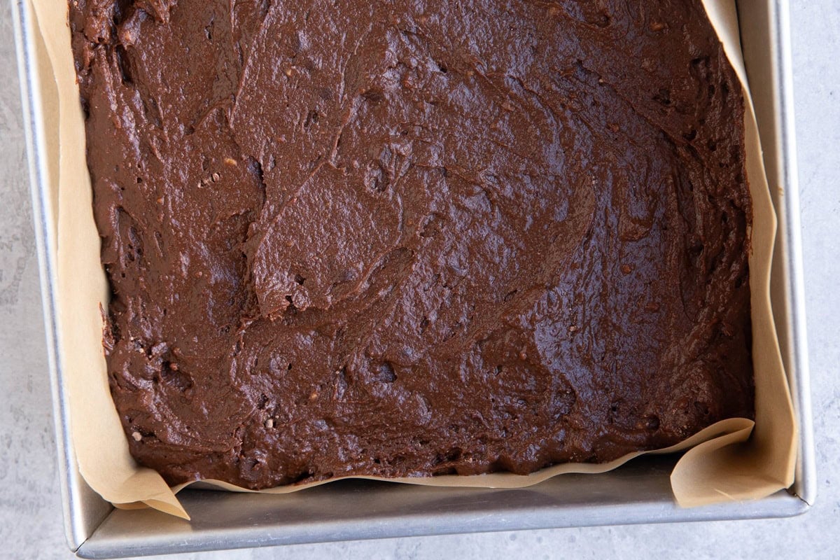 Chocolate cake batter spread in a 9-inch baking pan lined with parchment paper.