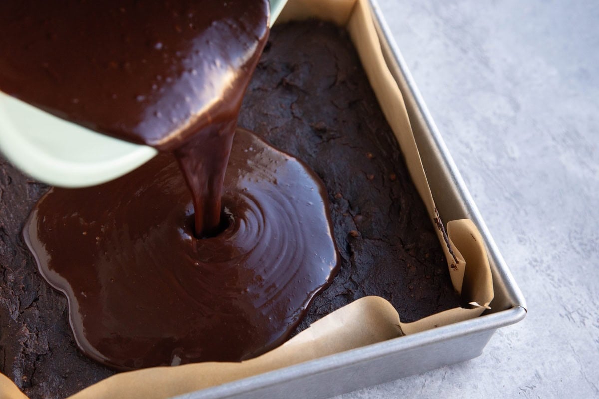 Pouring homemade ganache over a finished chocolate cake to use as frosting.