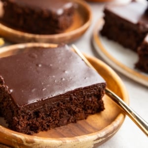 Two slices of pumpkin chocolate cake on wooden plates with a fresh pumpkin in the background and a golden fork, ready to serve.