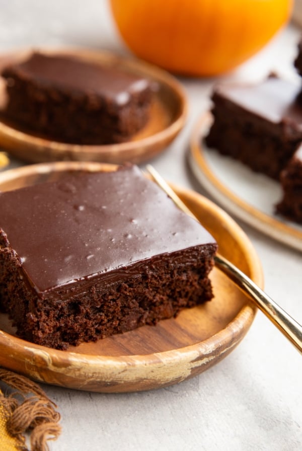 Two slices of pumpkin chocolate cake on wooden plates with a fresh pumpkin in the background and a golden fork, ready to serve.
