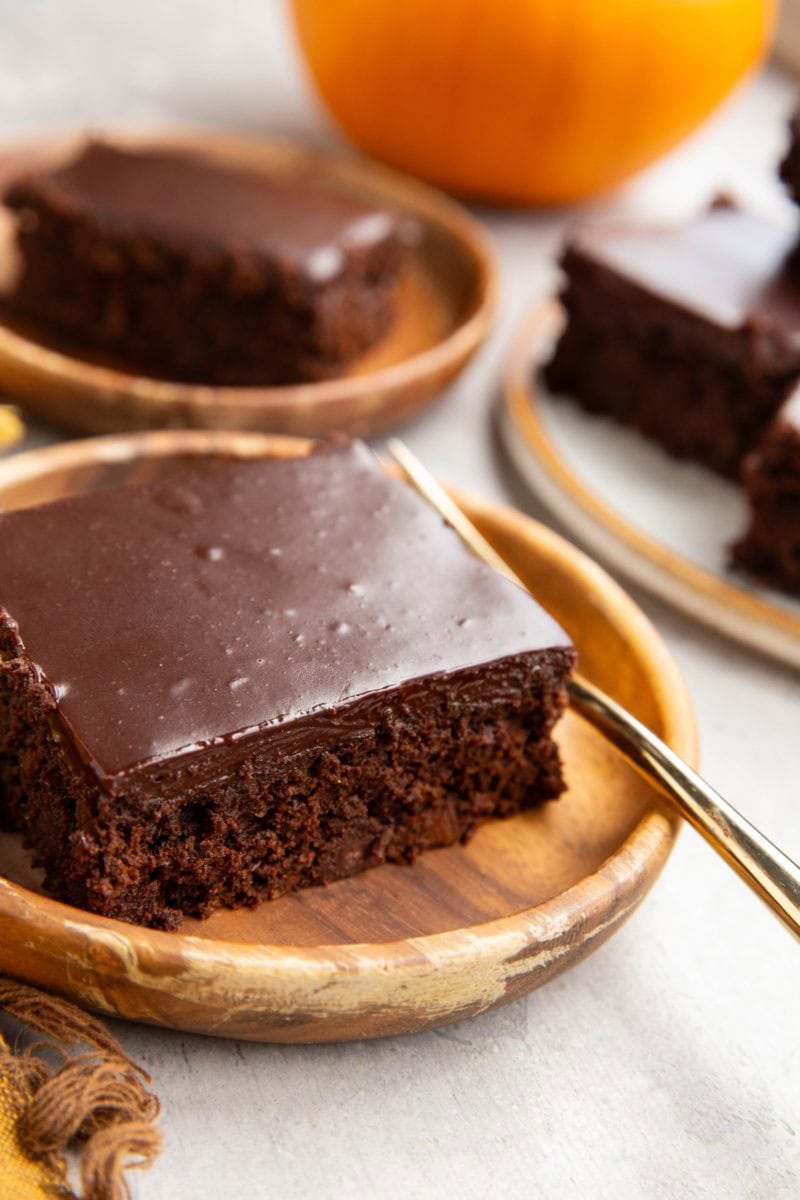 Two slices of pumpkin chocolate cake on wooden plates with a fresh pumpkin in the background and a golden fork, ready to serve.
