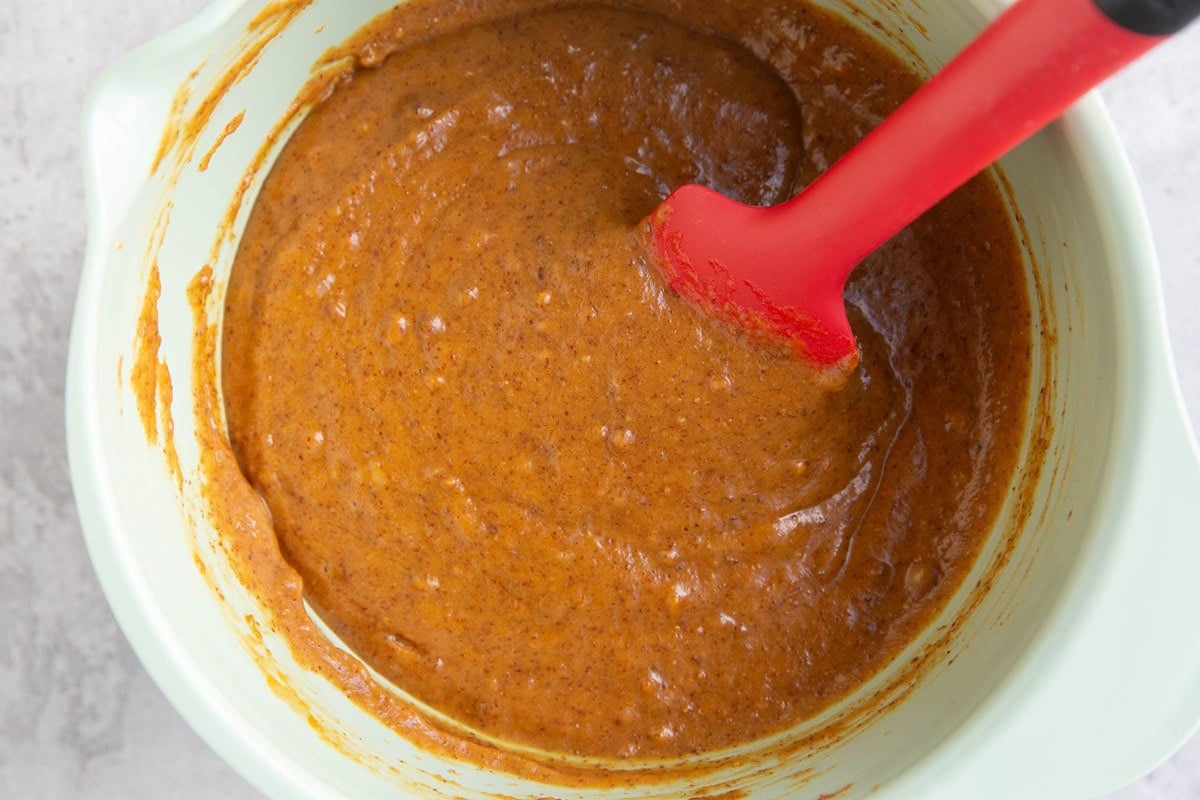 Wet ingredients for pumpkin chocolate cake in a large mixing bowl with a red rubber spatula inside.