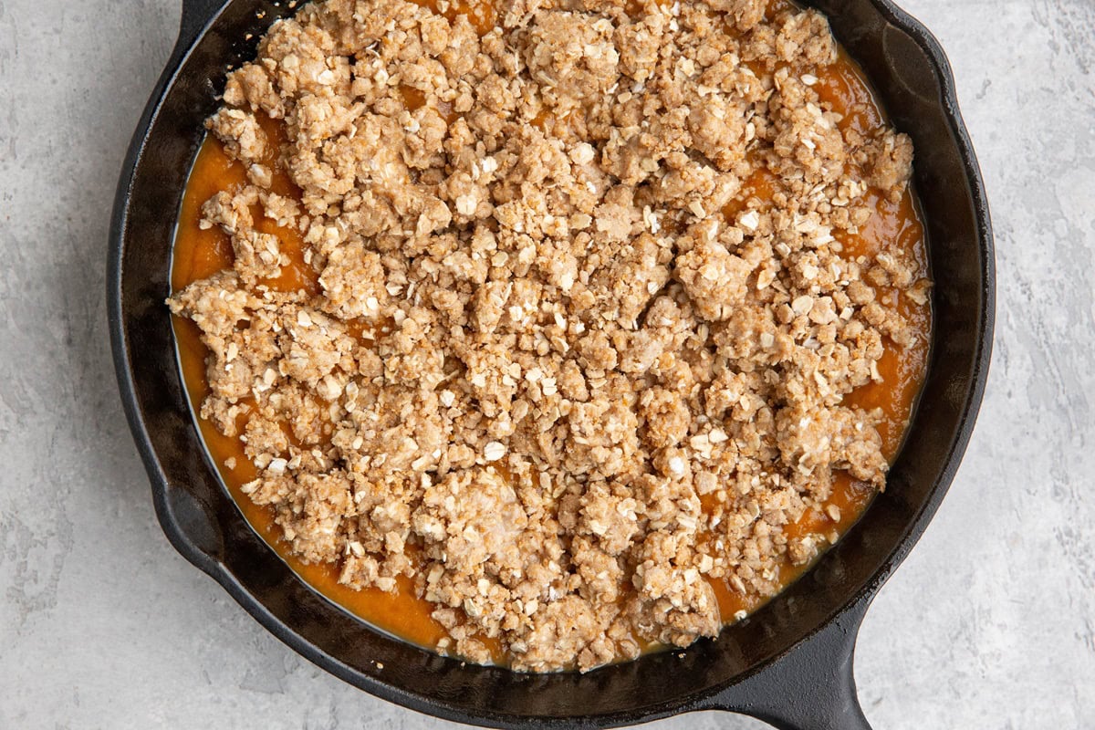 Cast iron skillet with a pumpkin layer and a crisp topping layer, ready to go into the oven to bake.