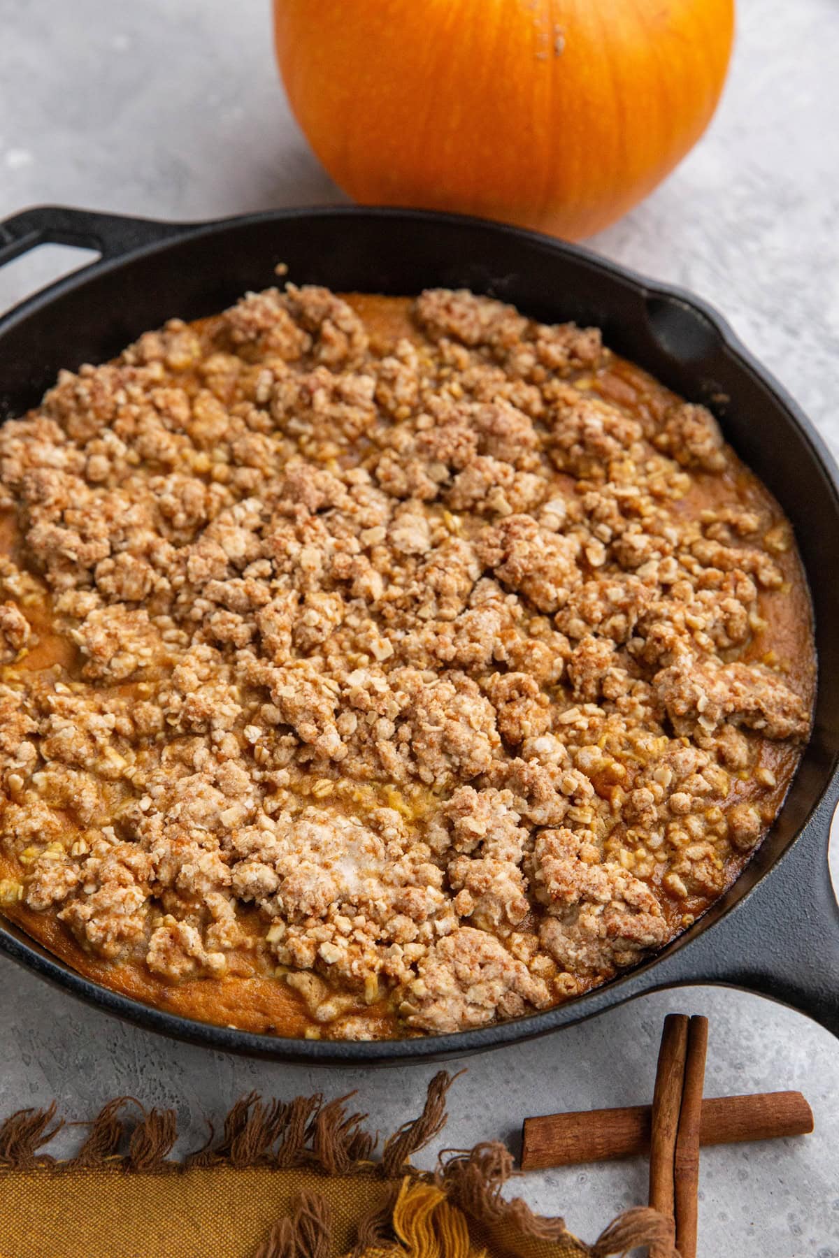 Pumpkin crisp in a cast iron skillet with a fresh pumpkin in the background.