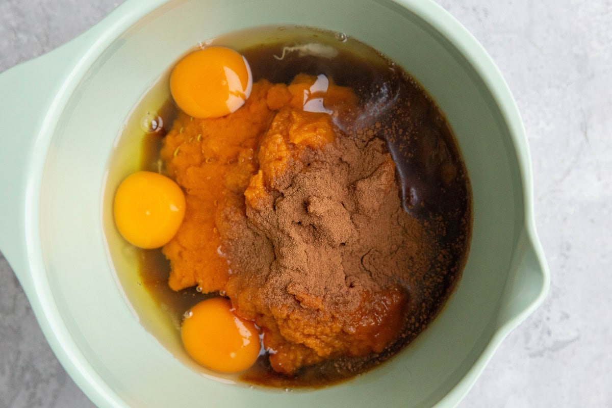 Mixing bowl with pumpkin puree, eggs, pure maple syrup, and pumpkin pie spice to mix up for pumpkin pie filling.