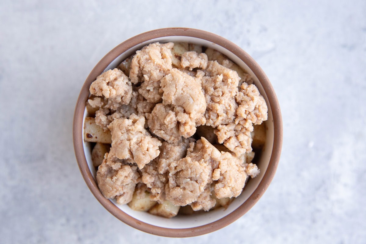 Ramekin full of chopped apples with crumble topping.
