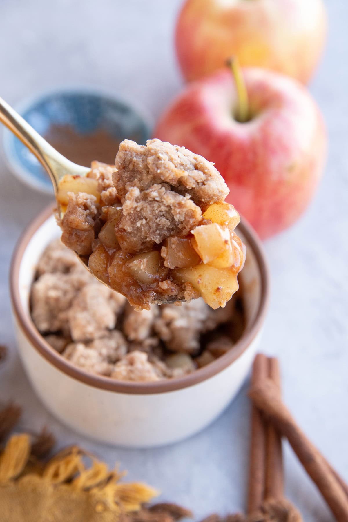 Spoonful of apple cobbler scooped out of a single-serve ramekin with fresh apples in the background.