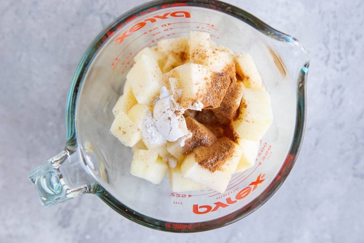 Measuring cup with chopped apples, cinnamon, flour, pure maple syrup.