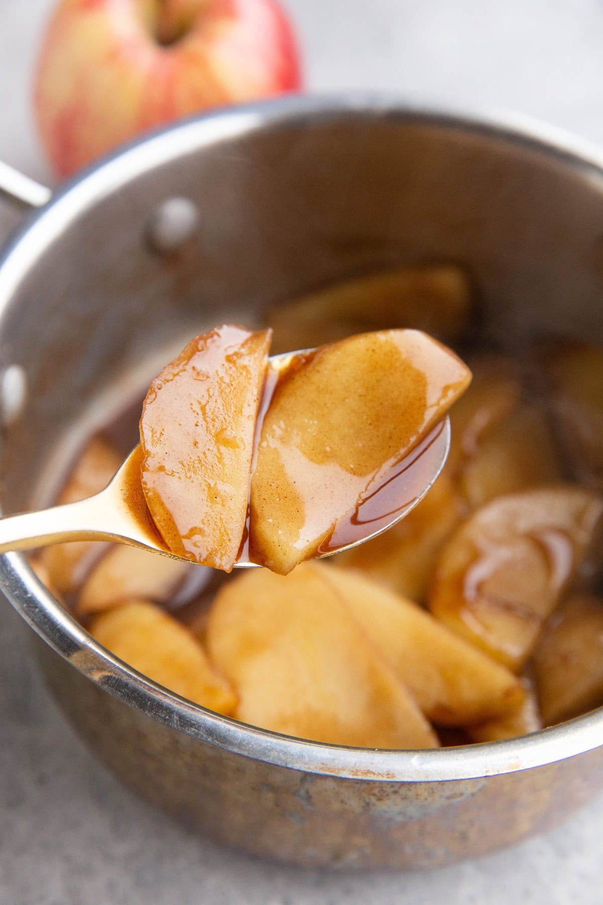 Spoon holding a couple of sliced apples that are softened to perfection with sauce around.
