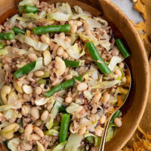 Wooden bowl full of wild rice salad with sauteed onion, cabbage, green beans, white beans, and more.