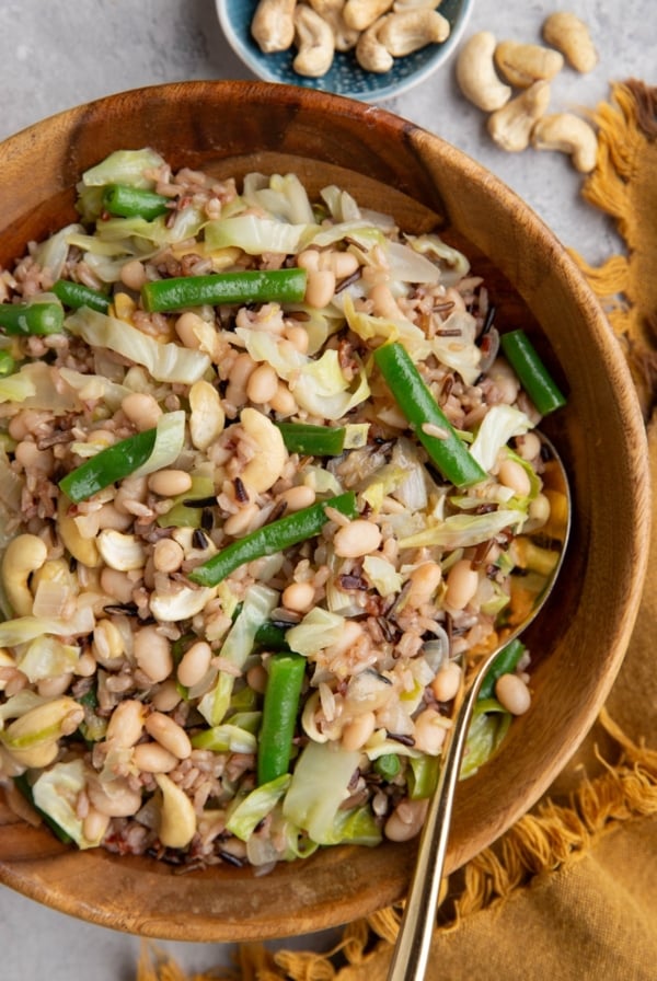 Wooden bowl full of wild rice salad with sauteed onion, cabbage, green beans, white beans, and more.