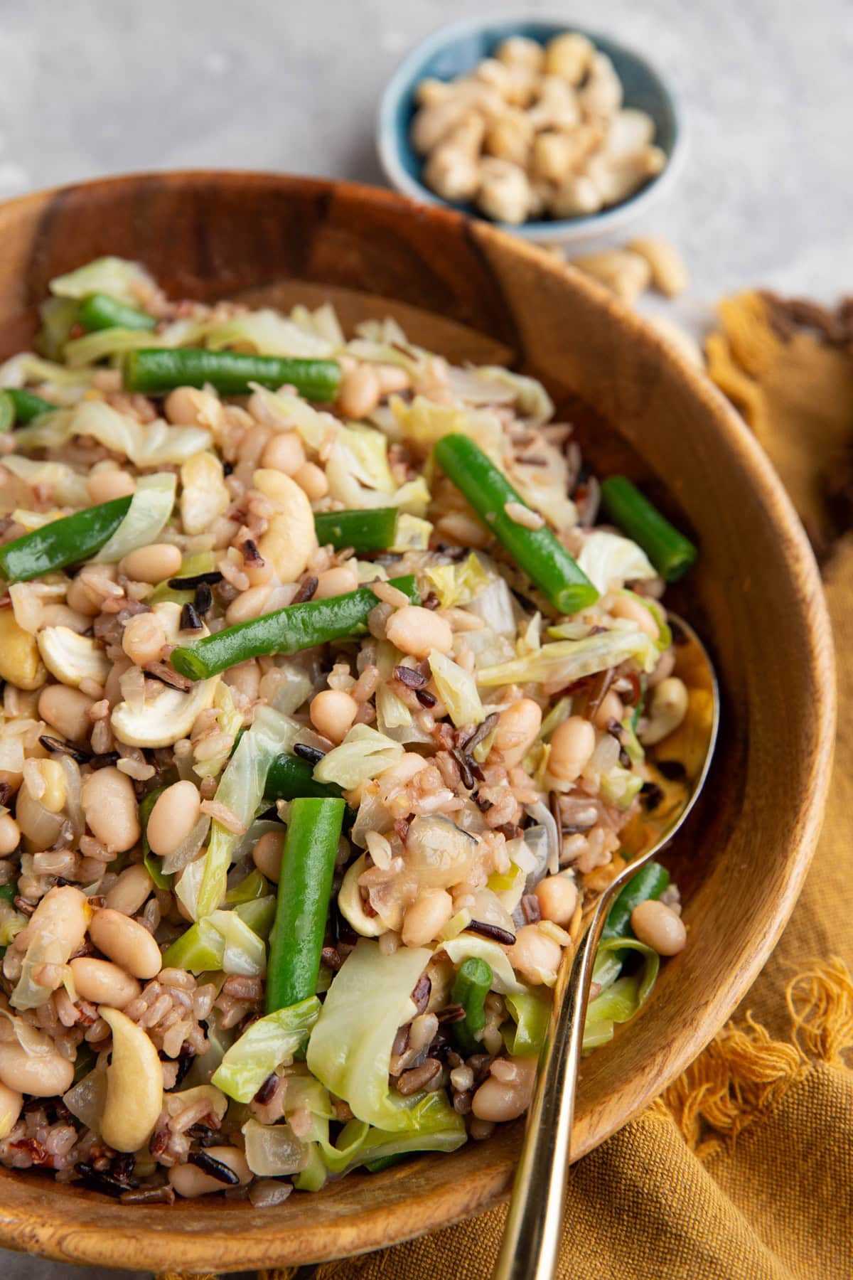 Wild Rice salad in a large wooden bowl with fresh veggies and a golden spoon. A small bowl of cashews in the background.