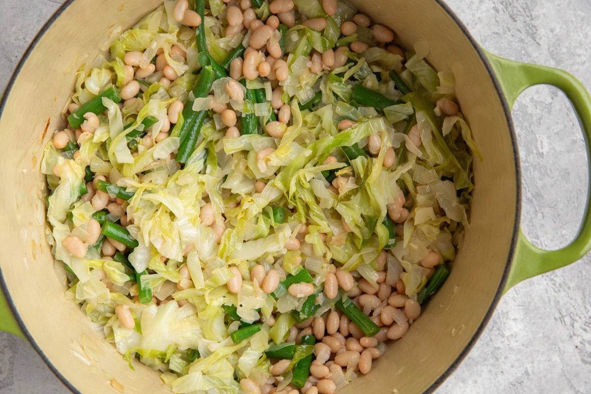 large pot of onion, cabbage, green beans, and white beans sauteed up to make wild rice salad.