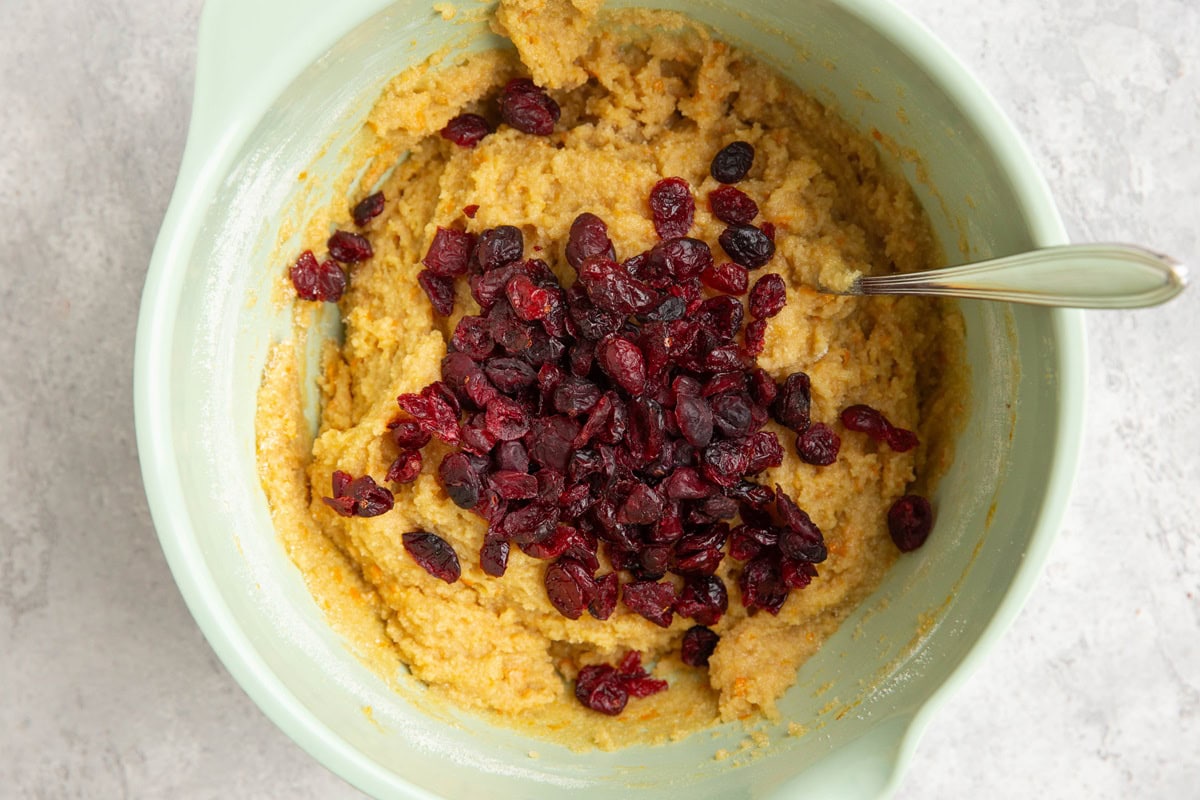 Mixing bowl with orange scone dough and dried cranberries on top, ready to be mixed in.