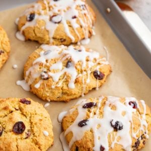 Baking sheet of cranberry orange scones drizzled with a glaze and a fresh orange in the background sliced in half.