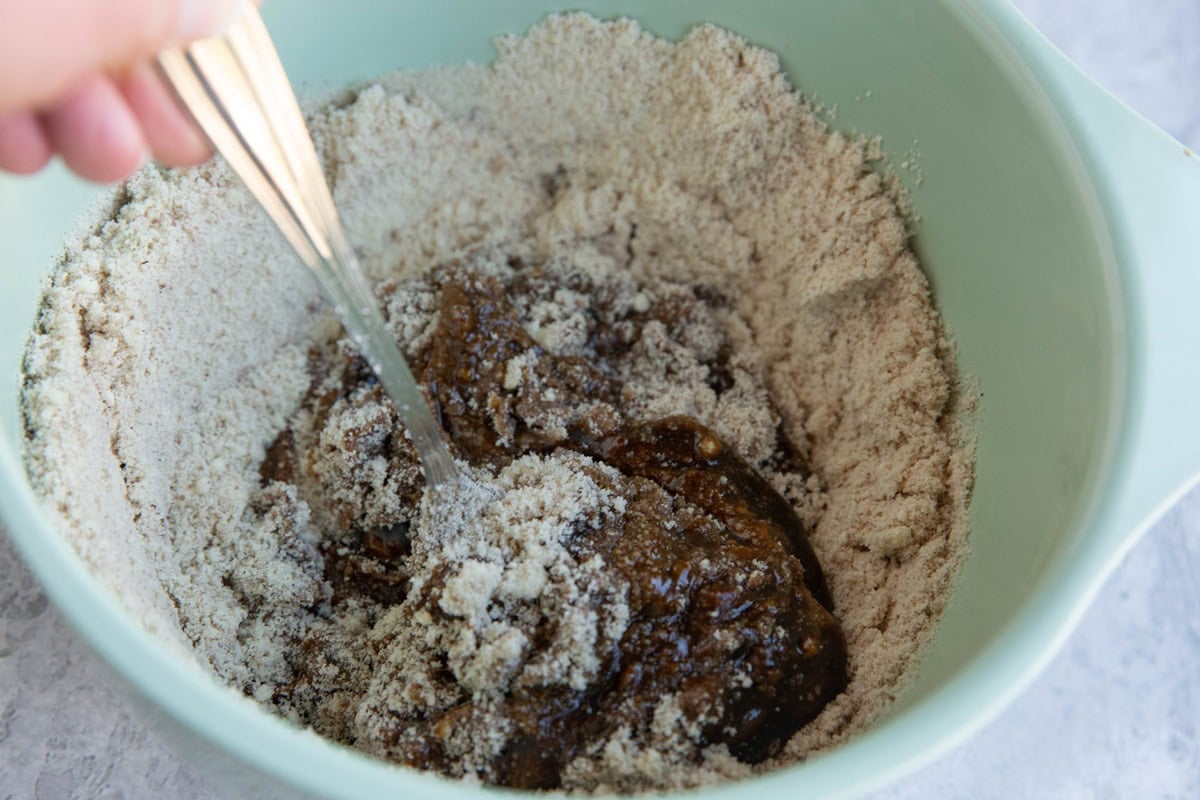 Hand stirring wet ingredients and dry ingredients together in a mixing bowl to make dough for gingerbread cookies.