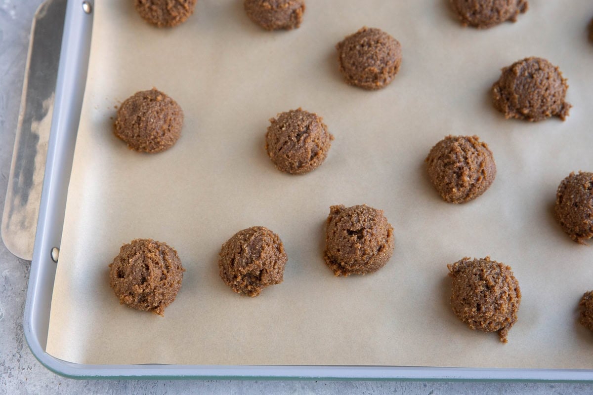 Ginger molasses cookie dough balls on a parchment-lined baking sheet.