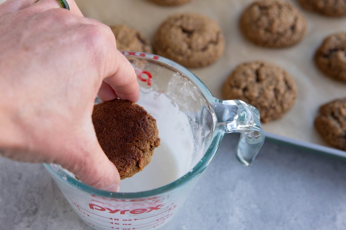 hand dipping a cookie into icing to make iced ginger molasses cookies.